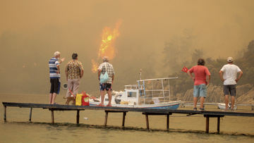 Tourists wait to be evacuated from smoke-engulfed Mazi area as wildfires rolled down the hill toward the seashore, in Bodrum, Mugla, Turkey, Sunday, Aug. 1, 2021