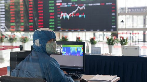 A worker wearing a protective suit reacts in front of an infrared temperature machine in the lobby of the Shanghai Stock Exchange building in Shanghai.