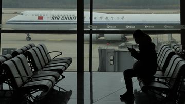 A passenger checks her phone as an Air China passenger jet taxi past at the Beijing Capital International airport in Beijing, Saturday, Oct. 29, 2022. China will drop a COVID-19 quarantine requirement for passengers arriving from abroad starting Jan. 8. The National Health Commission announced the change Monday, Dec. 26, 2022 as part of the latest easing of China&#x27;s once strict virus control measures. (AP Photo/Ng Han Guan)