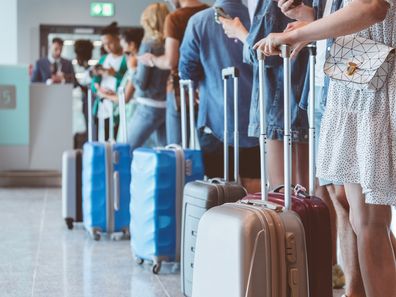 Travelers with luggage using smartphones while waiting in line for boarding at the airport. Focus on wheeled luggage.