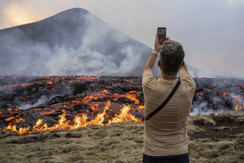 A man takes pictures as lava emerges from a fissure of the Fagradalsfjall volcano near the Litli-Hrútur mountain, some 30 kilometres southwest of Reykjavik, Iceland, Monday July 10, 2023.  