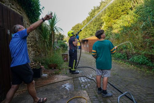 Local residents use garden hoses to assist fire crews from Cleveland Fire and Rescue services as they tackle a crop fire that swept over farmland and threatened local houses on August 11, 2022 in Skelton, England.