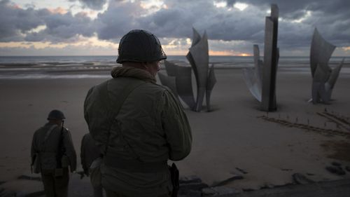 Two men in vintage US WWII uniforms walk toward the Les Braves monument at sunrise prior to a D-Day 76th anniversary ceremony in Saint Laurent sur Mer, Normandy, France, Saturday, June 6, 2020.