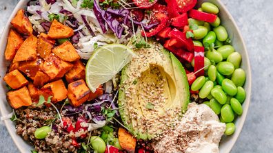 Overhead view of a colourful vegan bowl with quinoa, sweet potato, avocado, hummus and variety of veggies