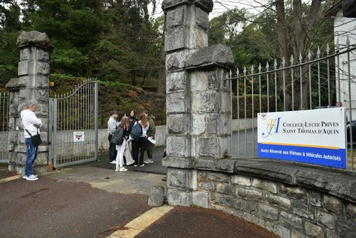 People stand at the entrance of the Saint-Thomas dAquin middle school in Saint-Jean-de-Luz, south-western France, where a teacher died after being stabbed by a student, on February 22, 2023  