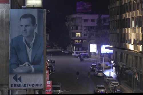 A giant banner of Syrian President Bashar Assad hangs on the facade of a building, as pedestrian walk through an the empty streets of  Damascus, Syria, Saturday, Dec. 7, 2024. (AP Photo/Omar Sanadiki)