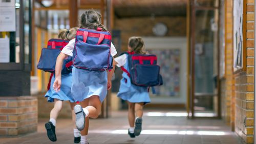 Rear view of excited students running towards entrance.  Girls are carrying backpacks while leaving from school.  Happy friends are wearing school uniforms.