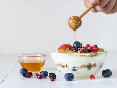 Bowl of yoghurt topped with mixed berries and honey.