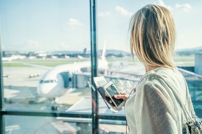 Young woman in airport waiting for flight sitting on bench with phone and passport in hands