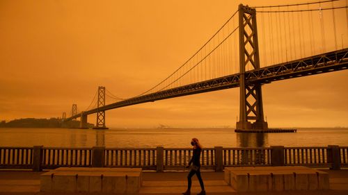 A woman walks along The Embarcadero under an orange smoke-filled sky Wednesday in San Francisco.