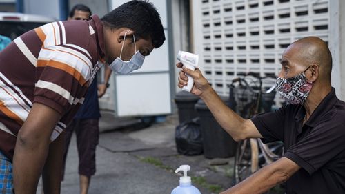 A migrant worker wearing protective face mask has his temperature checked by a security guard before leaving a factory-converted dormitory.