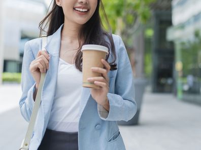 Stock image of a woman walking to her office with a coffee in her hand