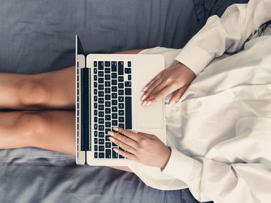 Woman working from home in bed with laptop computer