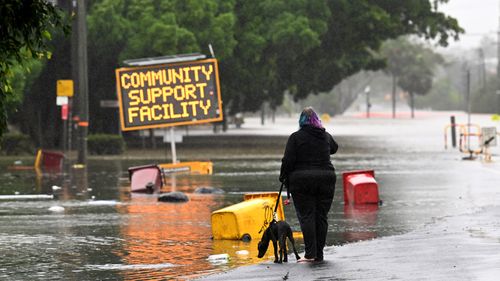 A woman walks her dog on a flooded road in Lismore, NSW