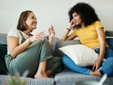 Women, friends talk and chat in a house having gossip, discussion and happy in a living room. Sofa, smile and female person on a couch having communication together in a home lounge with speaking