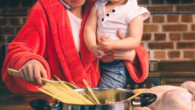 Tired mum cooking holding baby