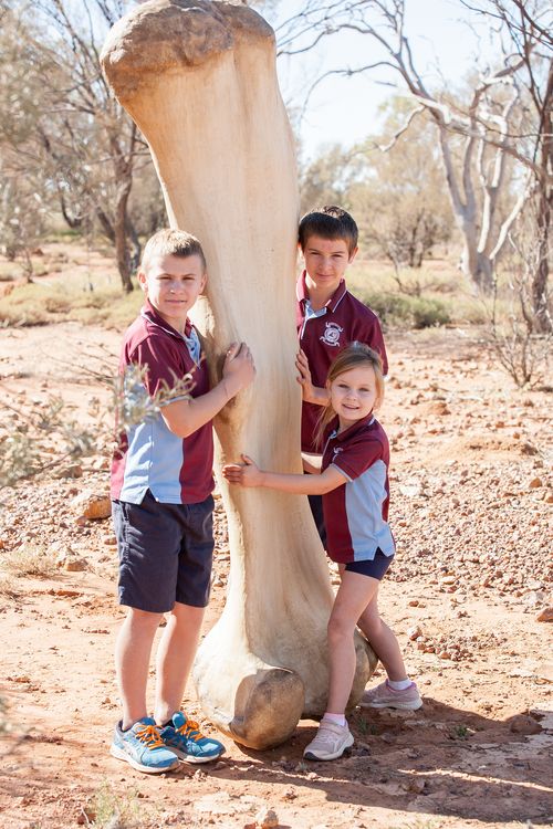 Children from Eromanga State School sizing up against a replica of Cooper's  Femur at the Eromanga Natural History Museum.