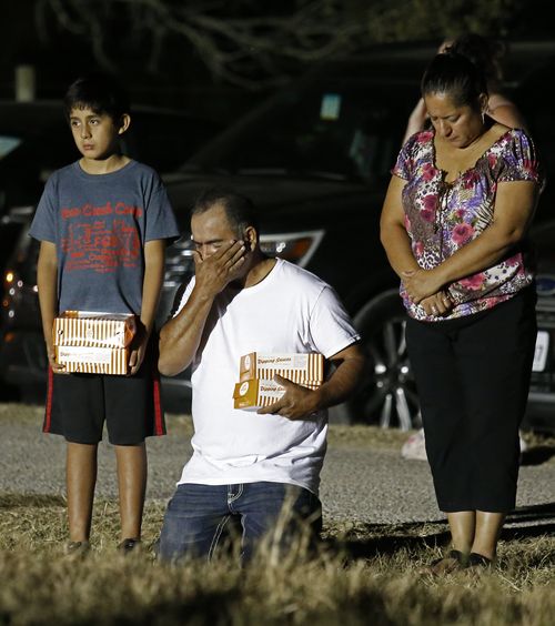 A man on his knees wipes tears from his face during a vigil a few blocks away from the shooting. (AAP)