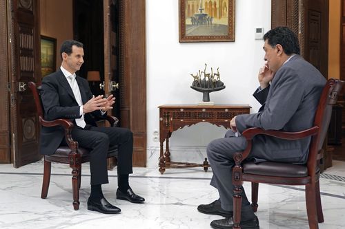 In this photo released Thursday, May 10, 2018, by the Syrian official news agency SANA, Syrian President Bashar Assad speaks during an interview with Alexis Papachelas, the the executive editor of the Greek Kathimerini newspaper, in Damascus, Syria. In the interview published Thursday, Assad said the current U.S. administration is inconsistent and nothing can be achieved with it in terms of ending the raging conflict in his country and that he hoped there is no direct confrontation between the U.S and Russia in Syria. (SANA via AP)