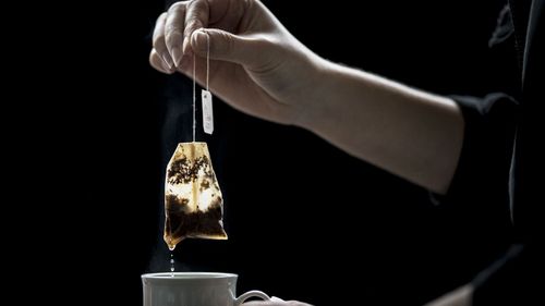 Stock image of a woman holding a tea bag above a cup of tea.