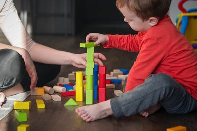 Mom and child, toddler son playing with colorful wooden bricks or blocks, enjoying time together at home. Creative indoors activities for kids.