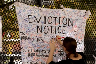 A woman signs an 'eviction notice' for President Donald Trump hanging on the security fence that surrounds the White House