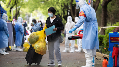 A villager carrying baggage is disinfected as she returns home after being quarantined due to local COVID cases found in Lianqin Village of Beicai Town in Pudong New Area, Shanghai on Tuesday, April 26, 2022. 