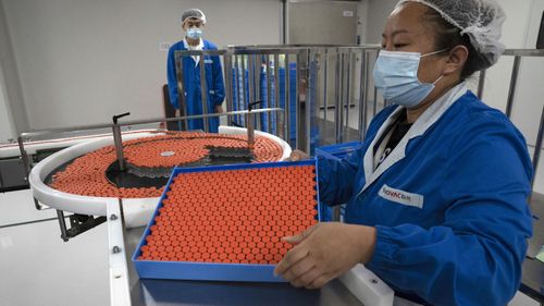 A worker feeds vials for production of SARS CoV-2 Vaccine for COVID-19 at the SinoVac vaccine factory in Beijing on Thursday, Sept. 24, 2020