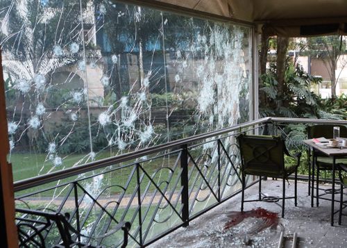 The bullet-riddled window of a cafe in the complex where dead bodies are clearly visible.