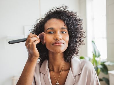 Beautiful curly young woman applying makeup in her bathroom in the morning.