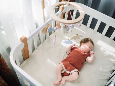 Newborn girl lies in white cradle with mobile above