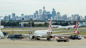 Passengers getting off an airplane at the Sydney Airport, with view of CBD in the background