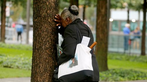 A woman weeps by herself as she leans against a tree during a ceremony marking the 17th anniversary of the terrorist attacks on the United States