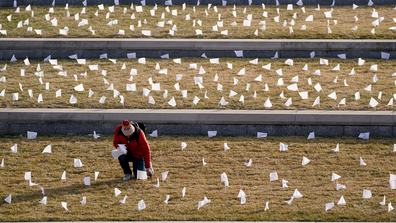A man places flags at the National World War I Museum and Memorial Tuesday, Jan. 19, 2021, in Kansas City, Mo. The 1,665 flags represent the area residents who died in the coronavirus pandemic and the display was part of a national memorial to lives lost to COVID-19. (AP Photo/Charlie Riedel)
