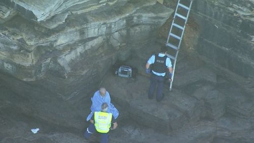 An emergency services member checks over a 91-year-old paraglider pilot after he crashed in waters off Sydney's northern beaches.