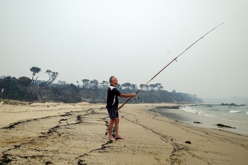 MALLACOOTA  AUSTRALIA - JANUARY 15:  Brett Mayor ,59, from Frankston fishes from the shore in Mallacoota on January 15, 2020 , Australia. The Princes Highway between Mallacoota and Orbost remains closed to public due to the risk of falling trees following the devastating bushfires that have swept through East Gippsland in recent weeks. ADF armoured vehicles have been travelling the stretch of road to bring supplies in to Mallacoota, after the coastal town was cut off by fire on New Years Eve, fo