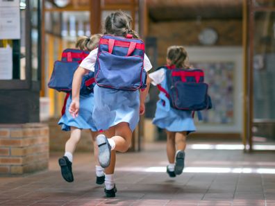 Rear view of excited students running towards entrance. Girls are carrying backpacks while leaving from school. Happy friends are wearing school uniforms.