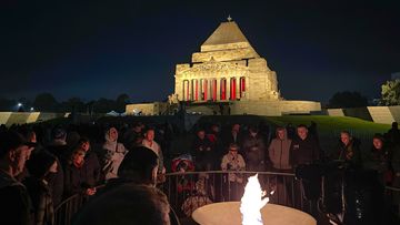 People gather around the flame during the ANZAC Day dawn service at the Shrine of Remembrance in Melbourne on April 25, 2022. 