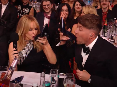 Kylie Minogue and Roman Kemp do a shoey during the 2024 Brit Awards