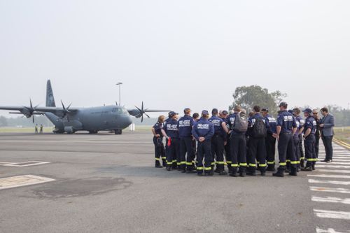 Firefighters assemble on the runway as they prepare to board an RAAF plane, in the background.