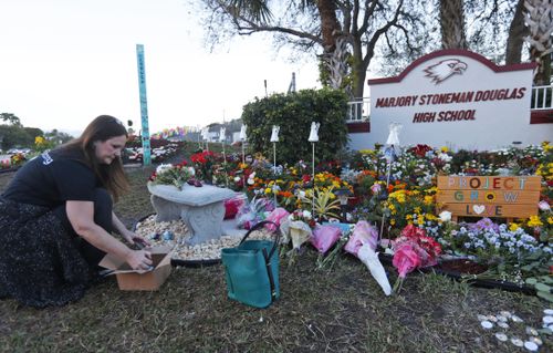 Suzanne Devine Clark, an art teacher at Deerfield Beach Elementary School, places painted stones at a memorial outside Marjory Stoneman Douglas High School during the one-year anniversary of the school shooting. 