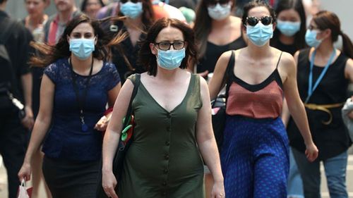 People wear face masks to protect from smoke haze as they cross a busy city street in Sydney, Australia. Smoke haze continues to hang over the city as bushfires burn across New South Wales.