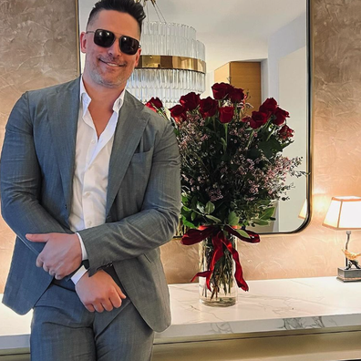 Joe Manganiello posing in a suit with a bunch of red roses in a vase.