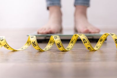 Women's legs on the scales, close-up of a measuring tape.