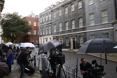 Media take shelter under umbrellas as they wait outside 10 Downing Street, the official home of the British Prime Minister in London, Friday, October 21, 2022. 