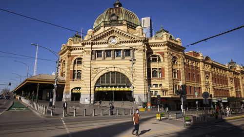 People crossing a quiet Flinders Street in Melbourne.