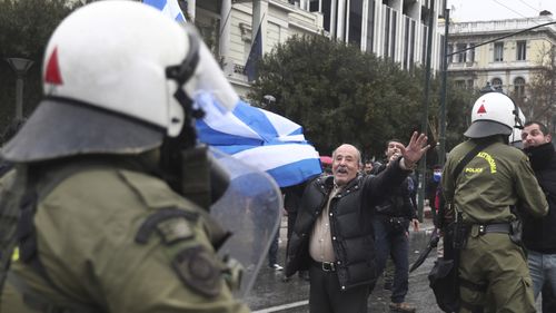 A man holding a Greek flag shouts slogans during clashes with riot police after a rally in Athens, Sunday, Jan. 20, 2019.