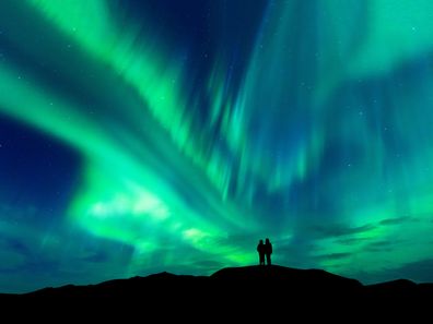 Aurora borealis in Finland with silhouette love romantic couple on the mountain.