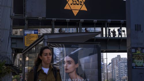 La gente camina a lo largo de un puente iluminado con una valla publicitaria que muestra una estrella amarilla de David leyendo "calidad"judío en alemán, se parece a lo que los judíos se vieron obligados a usar en la Alemania nazi, durante el Día anual de conmemoración del Holocausto en Ramat Gan, Israel.