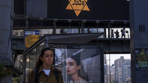 People walk along a bridge lit with a billboard showing a yellow Star of David that reads "Jude", Jew in German, resembling the one Jews were forced to wear in Nazi Germany, during the annual Holocaust Remembrance Day in Ramat Gan, Israel.